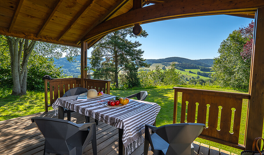 Vue extérieure depuis la terrasse en bois du chalet Charlay 21 en location au camping en Alsace Lefébure à Orbey